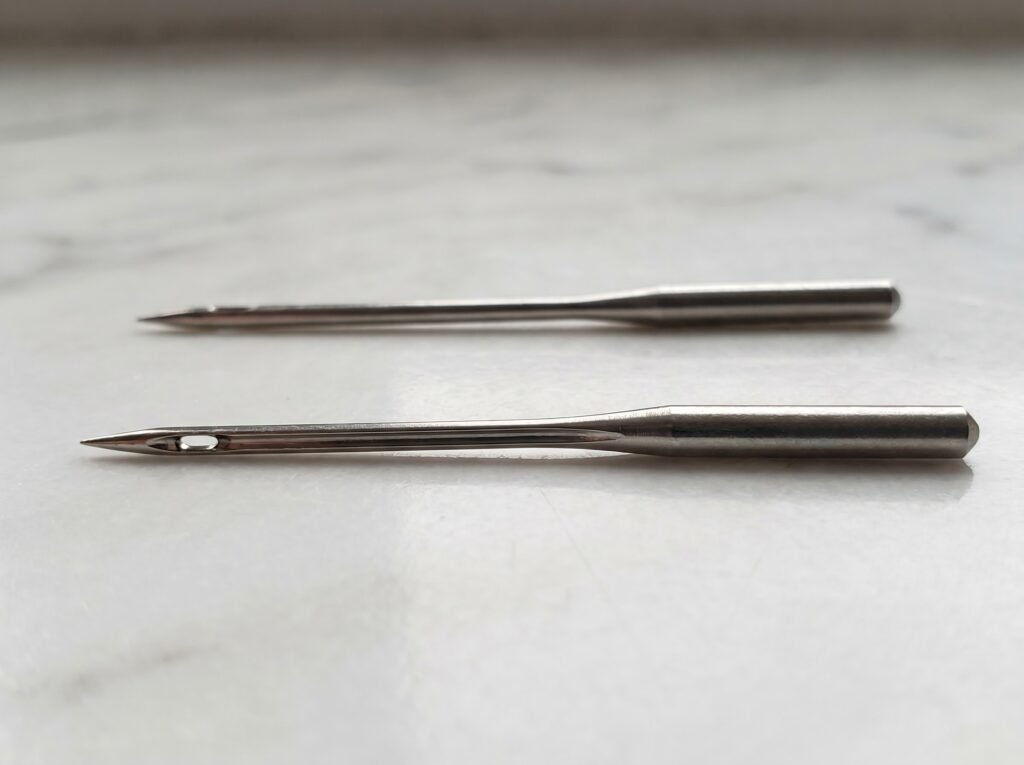 bent sewing machine needle compared to a straight replacement sewing machine needle rolled on a flat surface