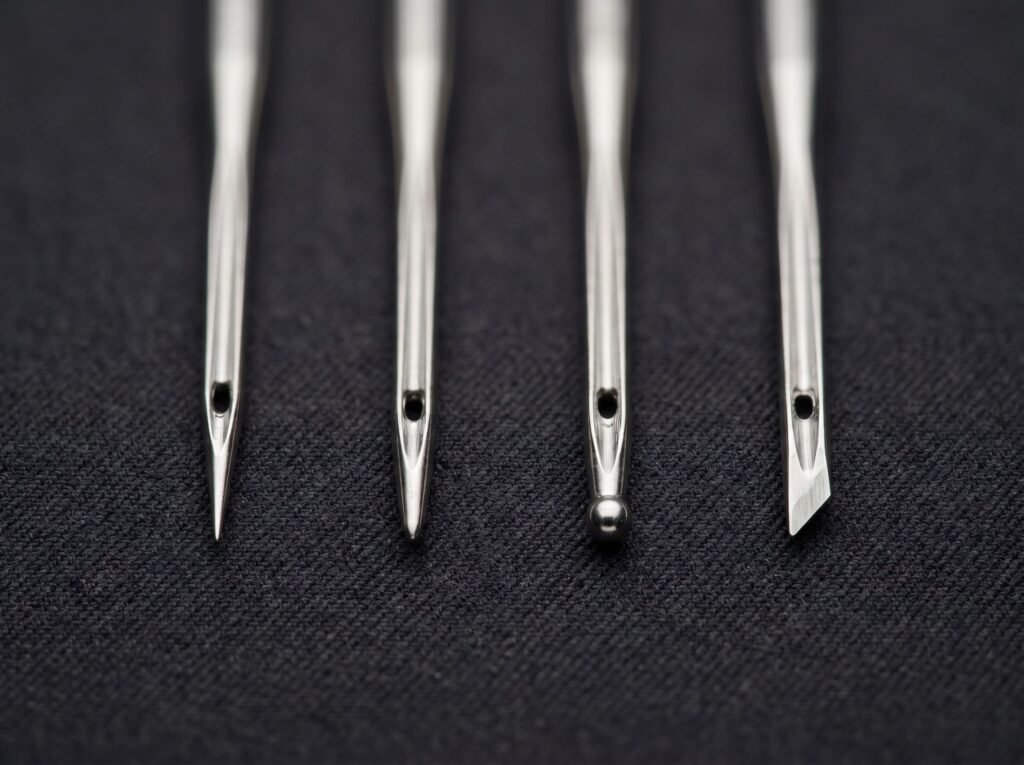 four sewing machine needle tip types side by side showing sharp, universal, ballpoint, and leather cutting points