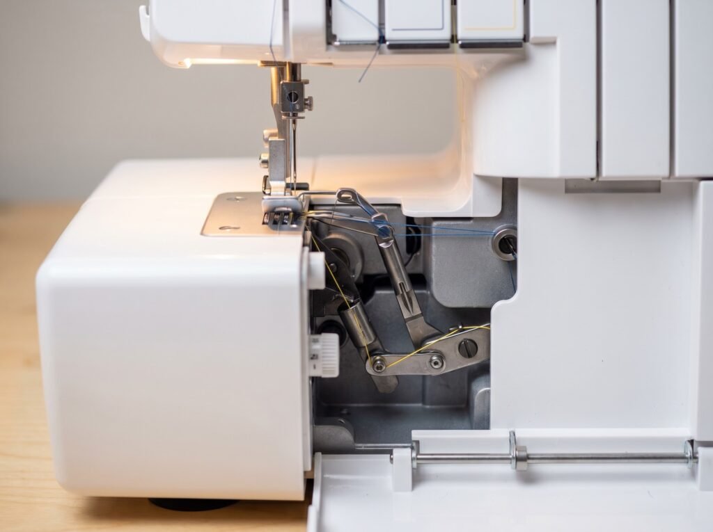Close-up of serger upper and lower looper arms with sewing machine needles installed and thread paths converging inside the machine
